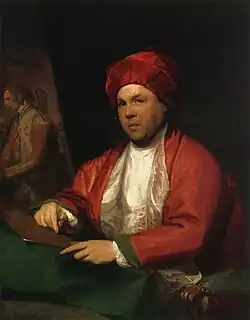 Peinture en couleurs. Un homme en vêtements et coiffe amples rouge et blanc est assis sur un fauteuil en velours vert. De trois quarts, il regarde vers le spectateur ; sa main droite tient une pointe sèche posée sur une plaque de cuivre, qu'il tient avec sa main gauche.