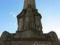 Vue contre-plongée de Jeanne d'Arc protégeant deux civils et un blessé de guerre.