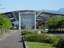 Photo sur l'entrée d'un bâtiment comprenant une grande porte vitrée et des toitures en acier.
