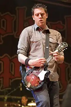 Homme caucasien aux cheveux bruns tenant une guitare.