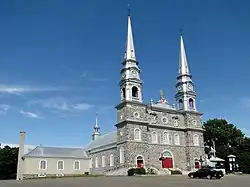 Photo d'une église grise avec deux hautes pointes et aux portes rouges.