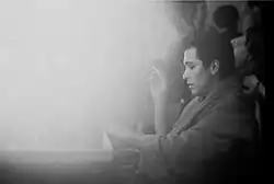 Photo en noir et blanc d'un homme brun vu de profil. Il est vêtu d'un peignoir et tient une cigarette.
