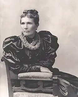 Portrait d'une femme pensive en robe noire satinée, assise.