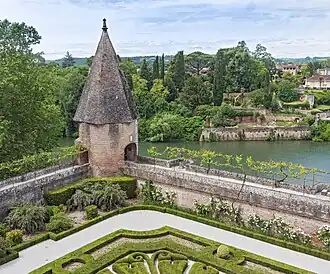 Tour à toit pointu en brique à l'angle d'une promenade sous pergola. En arrière-plan, le quartier de la Madeleine sur la rive droite du Tarn s'étage au dessus de jardins suspendus.