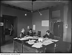Photo noir et blanc d'un bureau avec une table autour de laquelle quelques personnes sont en train de travailler.