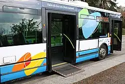 Photographie en couleurs d’un autobus bleu et blanc en stationnement avec la rampe d’accès déployée et les portes ouvertes.
