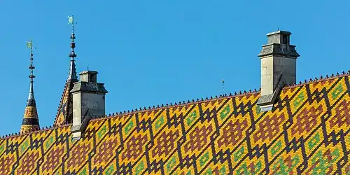Détails de toiture (tuiles vernissées, tourelles, cheminées) vus depuis les remparts, à l'arrière de l'Hôtel-Dieu, en fin d'après-midi.