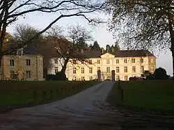 Photographie montrant la façade d'un château néo-classique entouré d'un portail et de quelques arbres.
