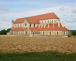 Photo d'une église monumentale de style gothique primitif en pierres blanches et jaunes et toits en tuiles rouges.