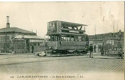 Tramway Saint-Denis - Paris au début du XXe&nbsp;siècle, à la barrière de la porte de la Chapelle. En arrière-plan, le pont Hainguerlot.