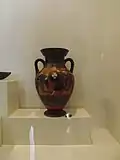 Une amphore rouge et noire avec une image centrale comportant des hoplites et la déesse Athéna avec un casque