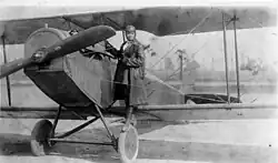 Photographie d'une femme en tenue d'aviateur debout sur une roue d'un biplan à l'arrêt.