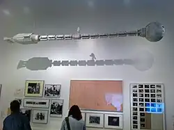 maquette d'une long vaisseau spatial tubulaire suspendu dans une salle d'exposition au-dessus de photos de tournage.