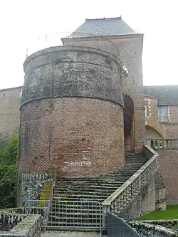 Photo couleur d'une courtine terminée par une tour de même niveau. Une autre tour en brique rouge couronnée d'un belvédère à garde-corps en fer forgé est contournée par un escalier qui mène des terrasses à la promenade et au jardin. Au-dessus, dépasse le toit en ardoise de l'aile dite de Stainville.