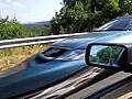 Rolling-Shutter-Effekt eines digitalen CMOS-Bildsensors. Der relativ zur Kamera in Ruhe befindliche Außenspiegel erscheint – wie der Hintergrund – unverzerrt. Beim Motion Blur würde das Fahrzeug hingegen gleichmäßig verzerrt im Bild erscheinen, so wie unter Umständen auch der Hintergrund verschmiert wirken.