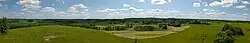 Dieses Farbfoto zeigt einen Panoramablick auf das in die dortige Landschaft eingebettete Dorf Radzie mit einem leicht bewölkten blauen Himmel und entstand 2015.