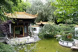 Chinesische Pagode mit geschwungenem Dach auf einer Steinplattform, die flach über ein Wasserbecken ragt